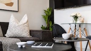 Een moderne woonkamer met een bank, twee zwarte salontafels, een bijzettafeltje van glas en een flatscreen televisie.
