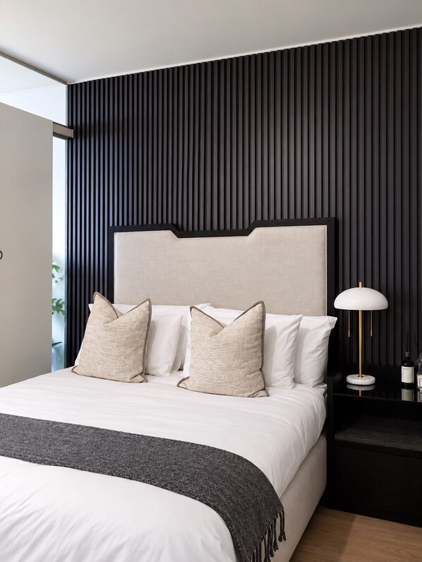 A modern bedroom with a large bed, a headboard, and a bedside table with a lamp.