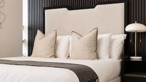 Een bed met hoofdeinde, meerdere kussens, een nachtkastje met een lamp en een vloerkleed.