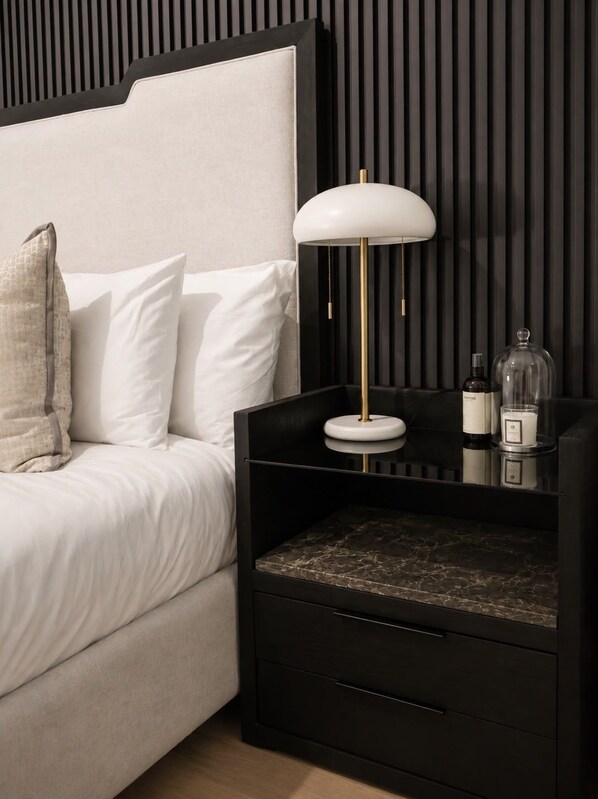 A modern bedroom with a bed, bedside table, lamp, and storage drawers.