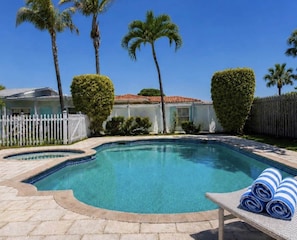 A swimming pool with a curved edge, surrounded by a white fence, palm trees, and a white picket fence. - BEACHaus Cottage -Pool- 2 Blocks from Beach+Pier (Deerfield Beach)