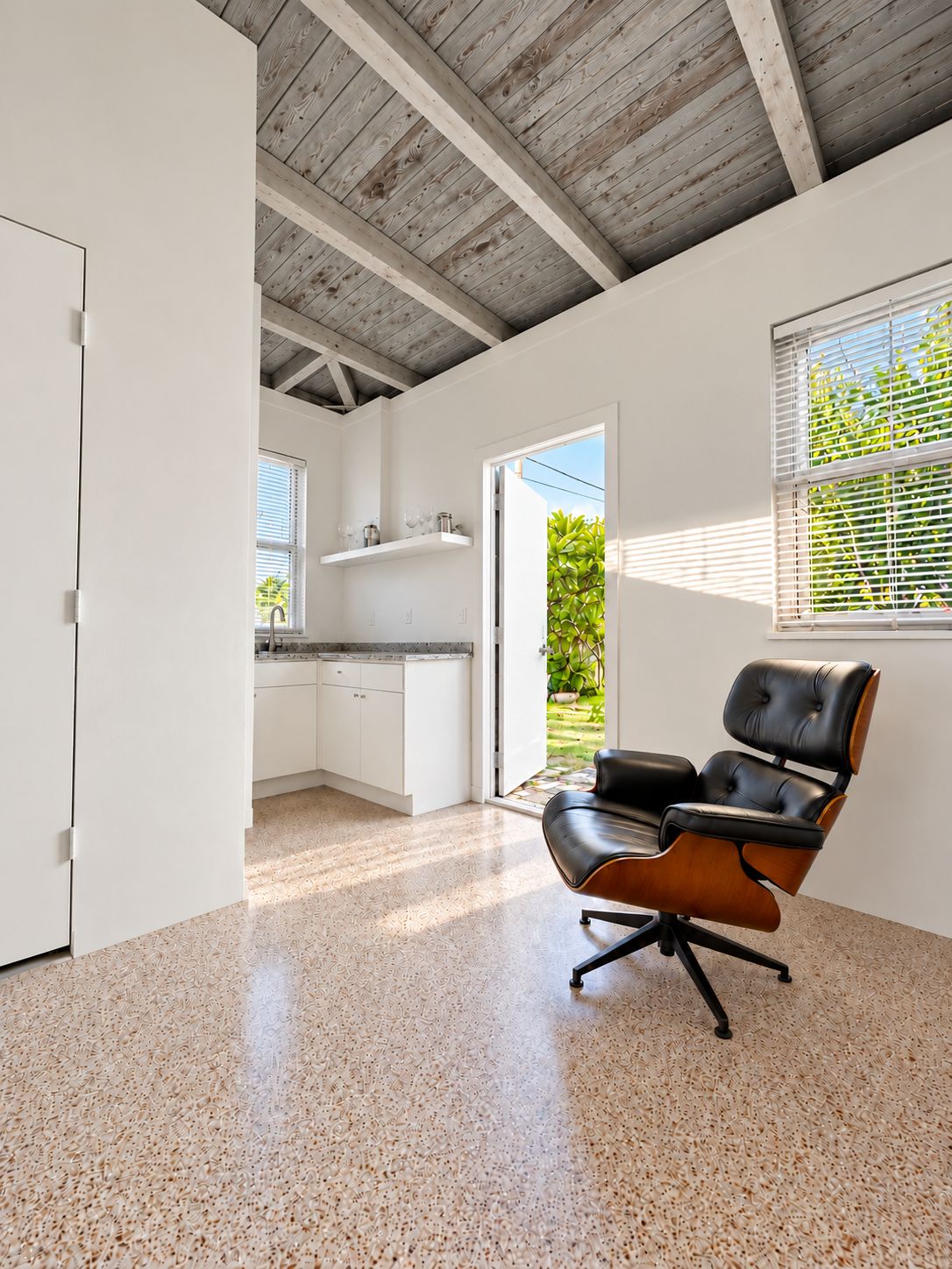 A spacious room with a kitchen area, a dining chair, and a view of greenery outside.