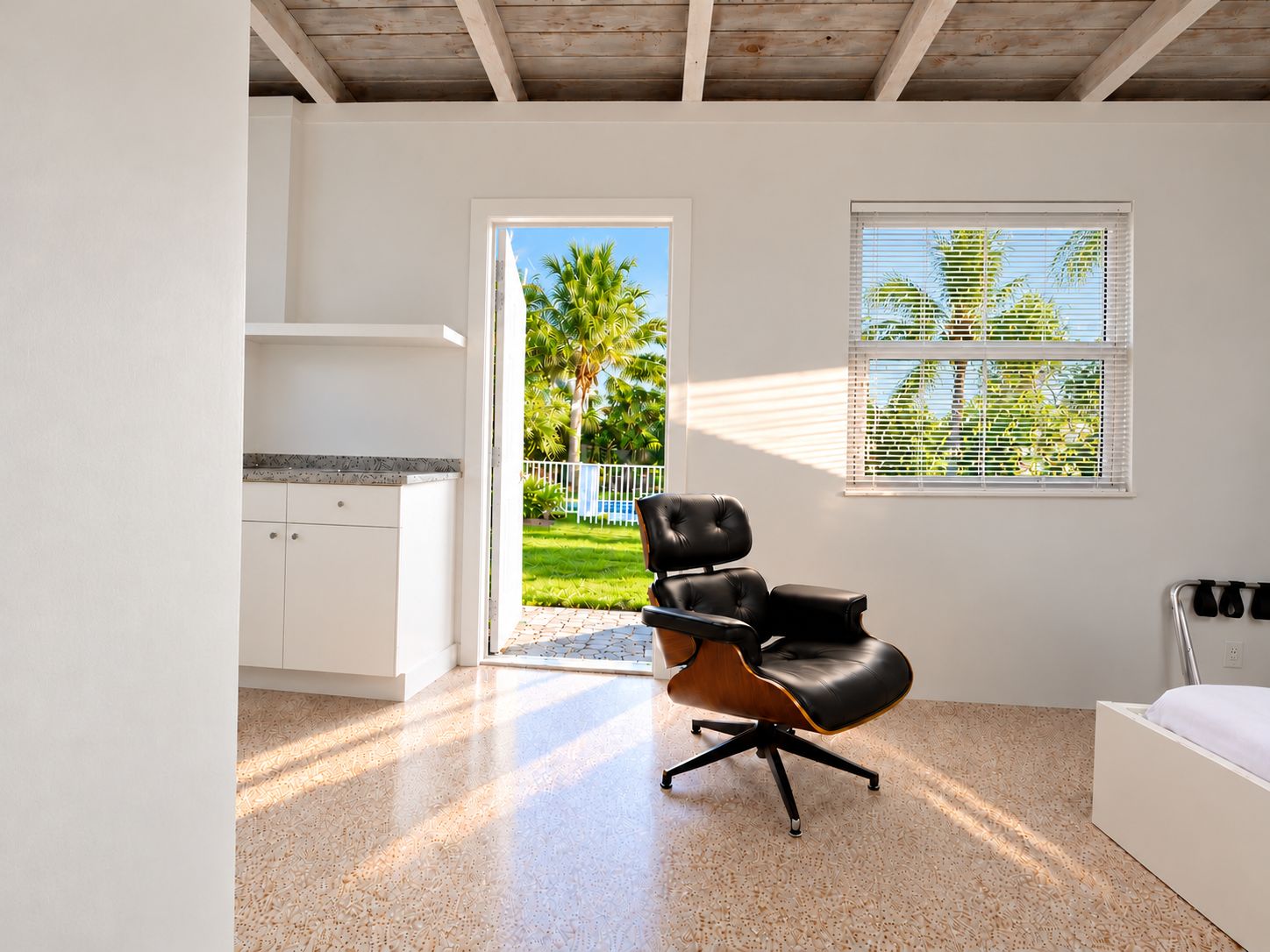 A modern room with a kitchen area, a large window with blinds, and a seating area with a chair.