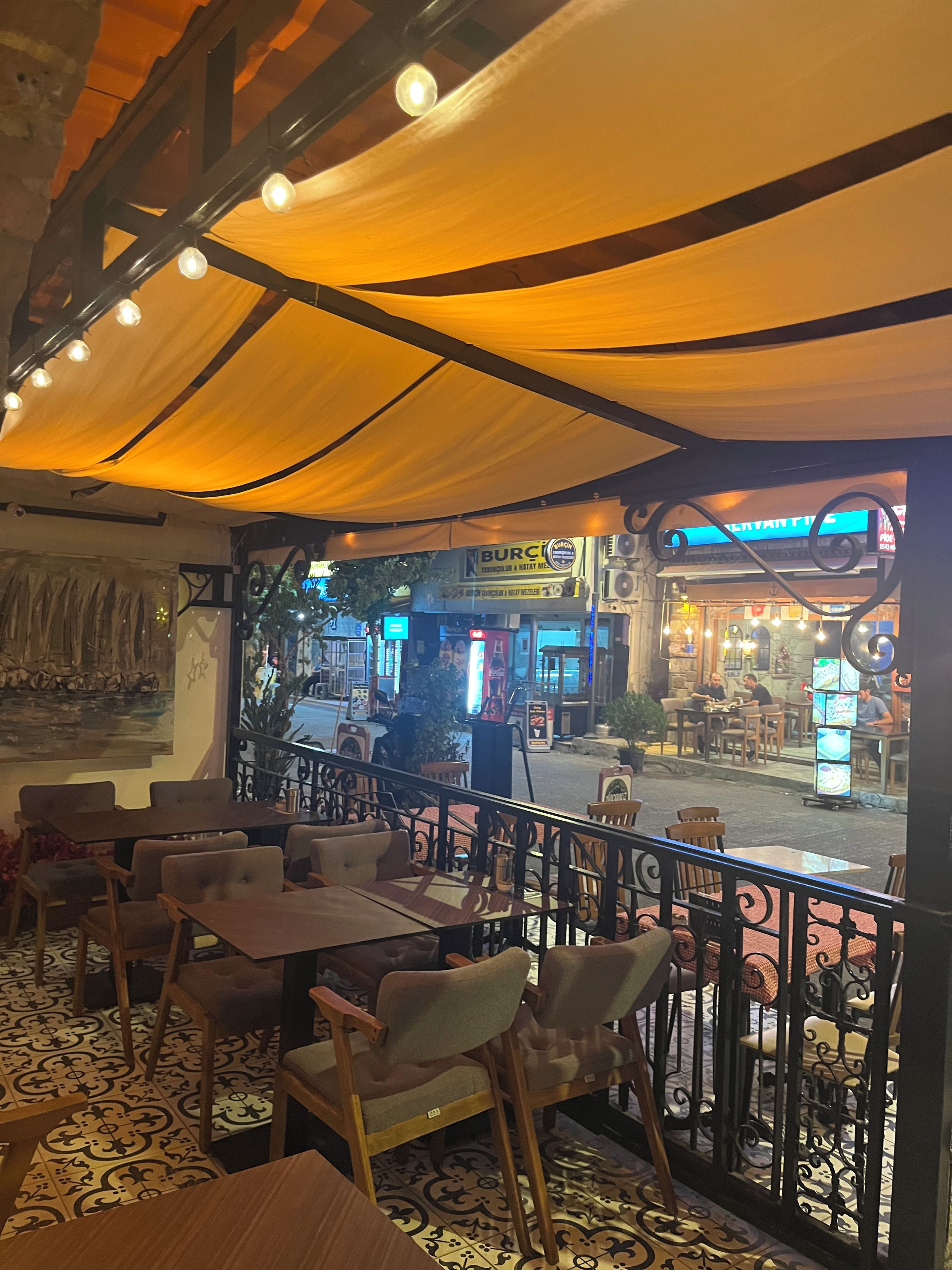 Un comedor interior con mesas y sillas, vista a la calle y un letrero de restaurante.