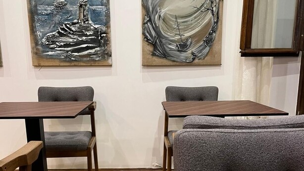 A room with two wooden tables, grey upholstered chairs, and a sofa.