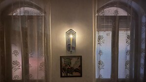 A room with two windows featuring lace curtains, a wall-mounted light fixture, and a framed picture.