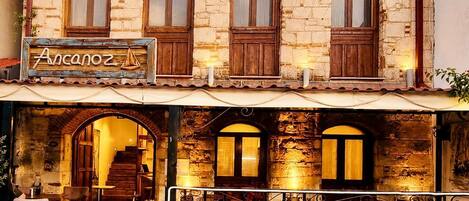 A building with a stone facade, a sign reading 'Ancanoz,' and an outdoor seating area with tables and chairs.