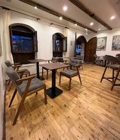 Un comedor con mesas y sillas de madera, suelo de madera y vistas por una ventana.