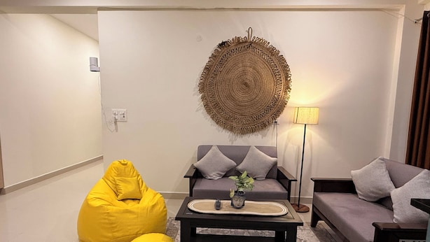 Una sala de estar con un sofá, un sillón de peluche amarillo, una mesa de centro y una lámpara.
