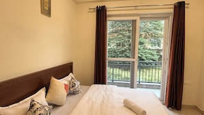 Una habitación de hotel con una cama, un ventanal con cortinas y vistas a la vegetación.