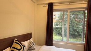 Habitación de hotel con cama, ventana con cortinas y vista a zonas verdes.
