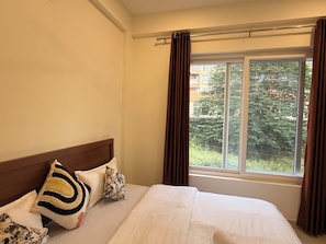Ein Hotelzimmer mit einem Bett, einem Vorhangfenster und Blick auf Grünfläche.