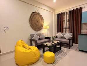 Ein Wohnzimmer mit zwei Sofas, einem gelben Sitzsack, einem Couchtisch, einer Wanddekoration und einem Vorhang.