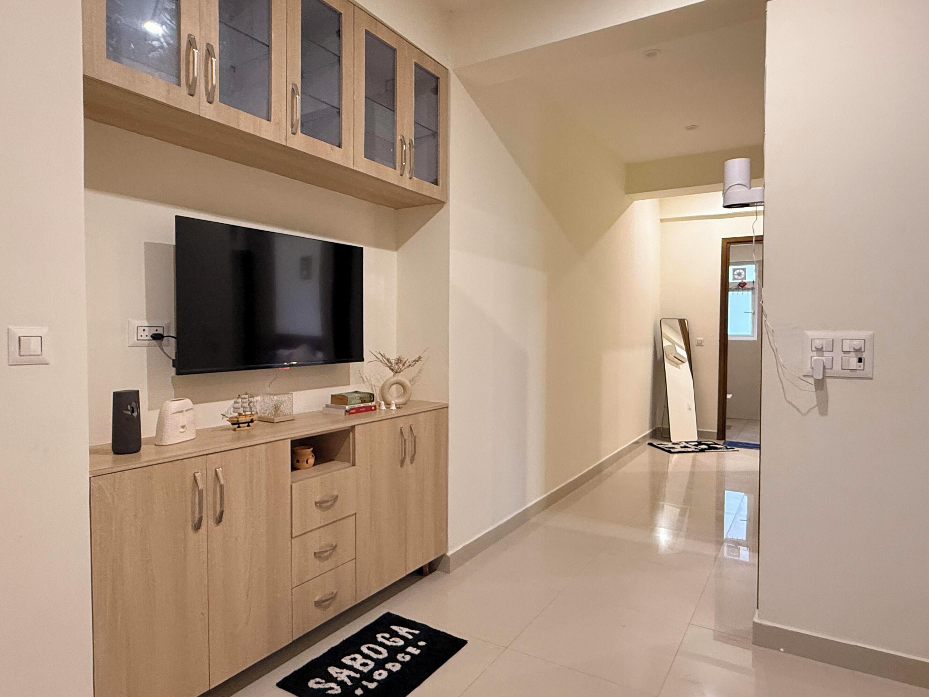A hallway with a flat-screen TV mounted above a wooden cabinet, a doormat on the floor, and a door leading to another room.