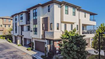 A modern multi-story residential building with a garage, a balcony on the upper floor, and a well-maintained front yard with landscaping.