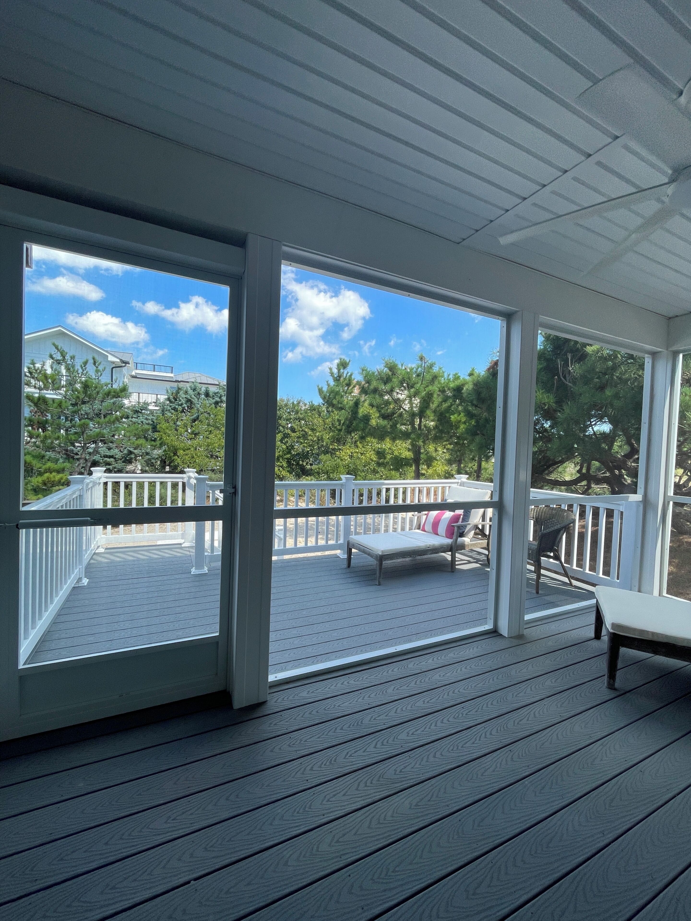 A covered outdoor deck with a white railing, a bench, and a view of a residential area with trees and houses.