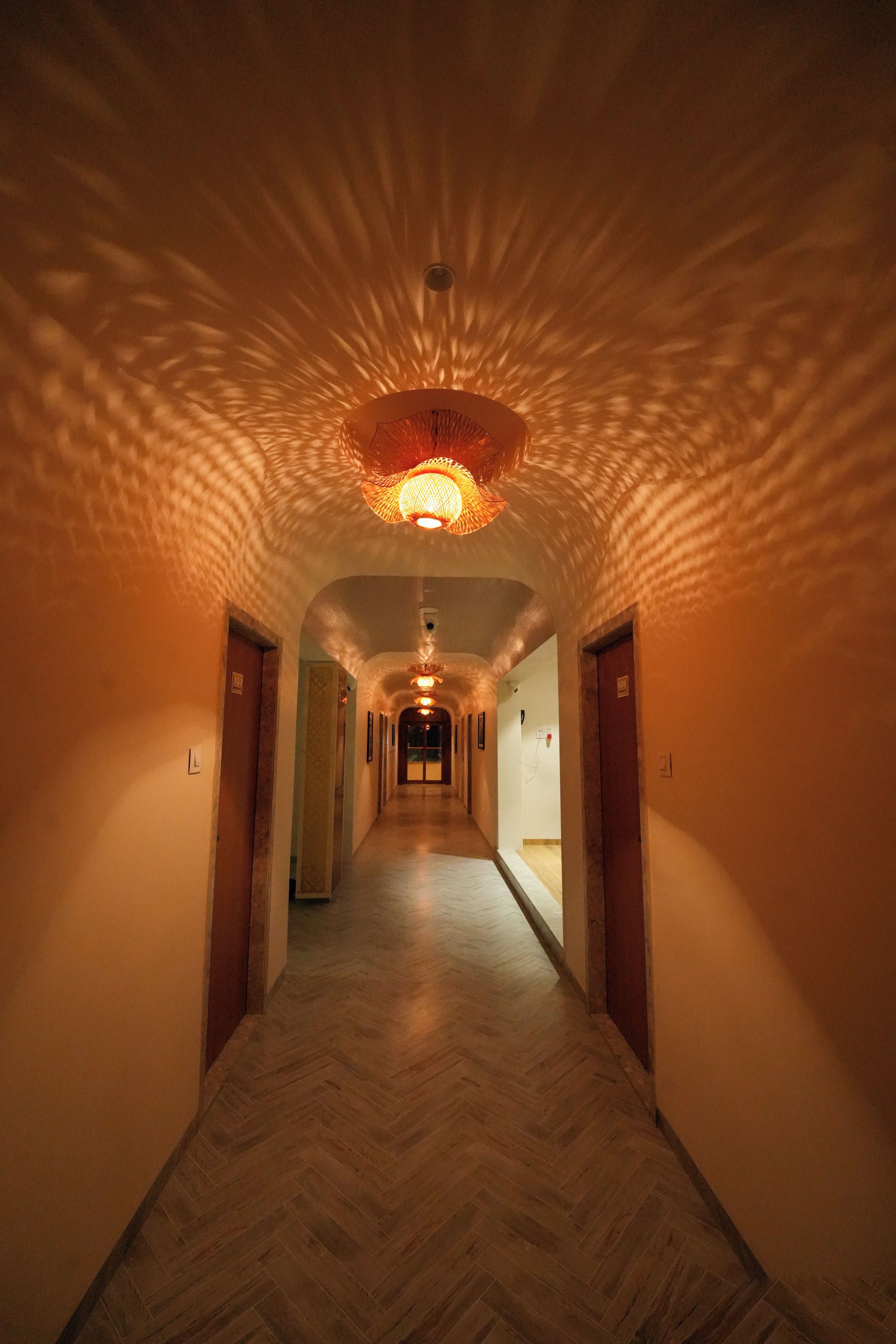 A hotel hallway with a herringbone floor, a central light fixture, and doors labeled with numbers.