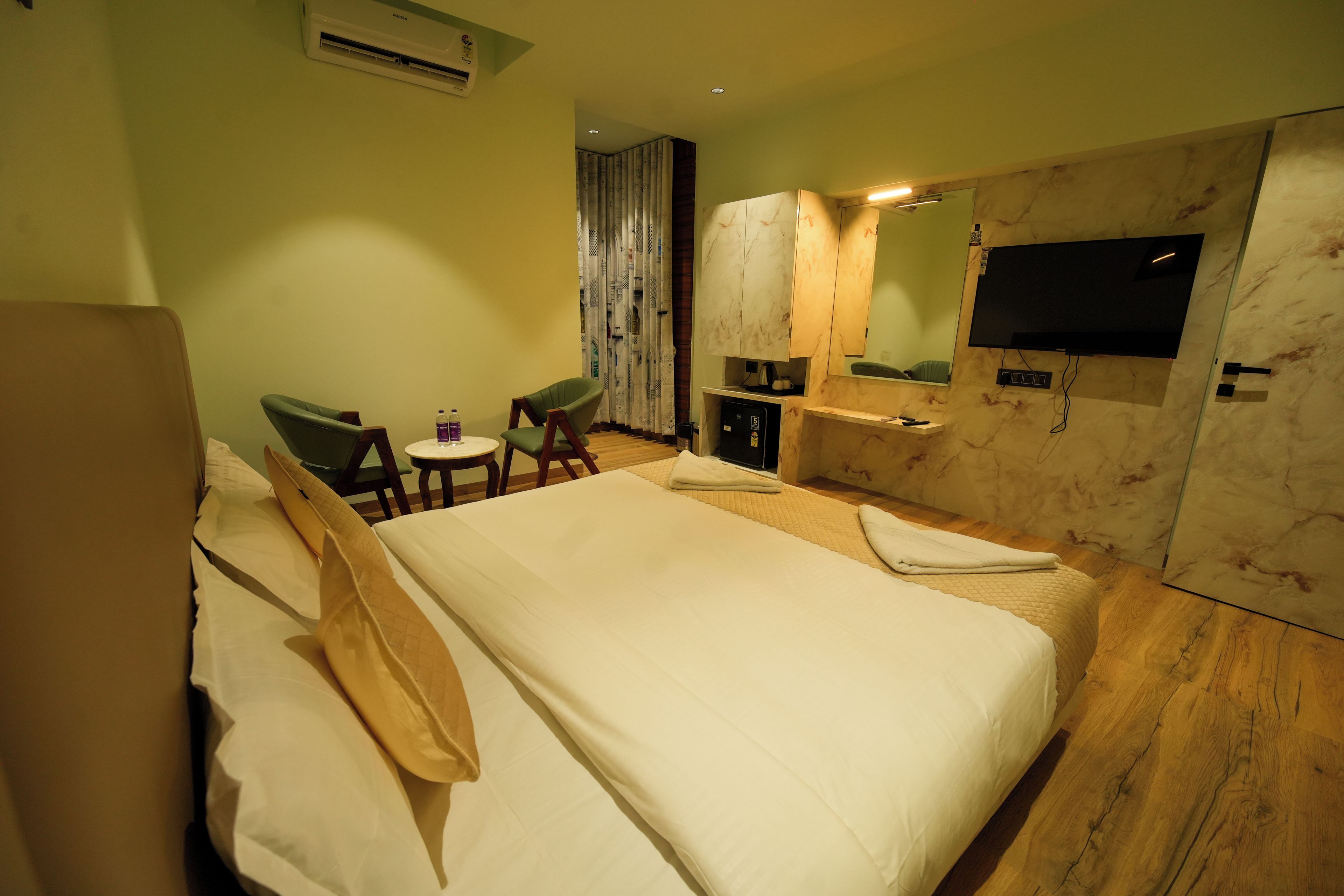 Ein Hotelzimmer mit einem Bett, zwei Stühlen, einem kleinen Tisch, einem Fernseher und einer Minibar.
