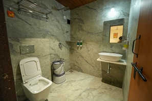 Et badeværelse med toilet, bidet og håndvask, marmorvægge og et brusehoved.