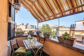 A balcony with a striped awning, potted plants, a table with chairs, and a view of the cityscape. - Domus Heroas near Vatican (Rome)