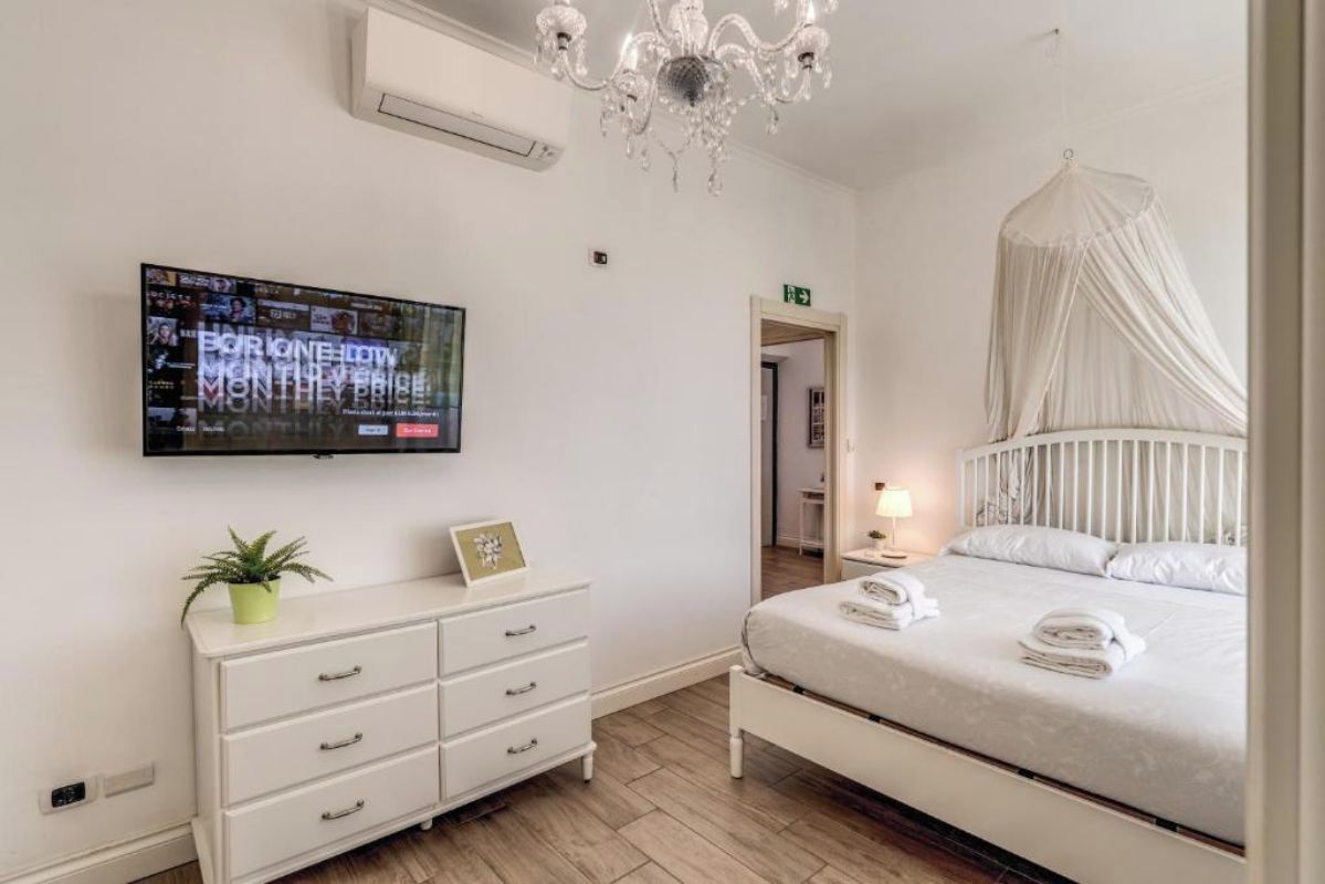A hotel room with a bed, bedside table, lamp, TV, and a white dresser.