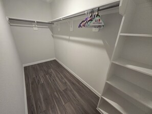 Um closet espaçoso com piso de madeira, paredes brancas e uma barra de metal para pendurar roupas.