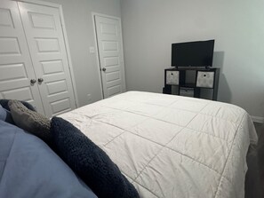 Une chambre à coucher avec un lit, deux portes blanches, une commode et un téléviseur posé sur un meuble.
