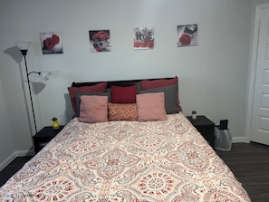 Quarto com colcha estampada, mesa de cabeceira com abajur e decoração nas paredes.