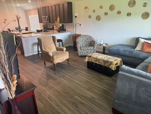 Ein modernes Wohnzimmer mit einer Couch, einem Sessel, einem Hocker und einem gemusterten Sessel.