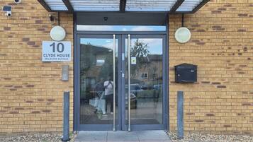 The entrance to a building with a numbered address sign, a glass door, and a brick facade.