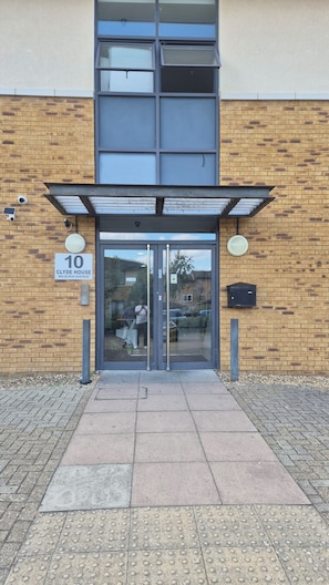The entrance to a building with a numbered address sign, a glass door, and a brick facade. - Milburn Residents (Oldbrook)