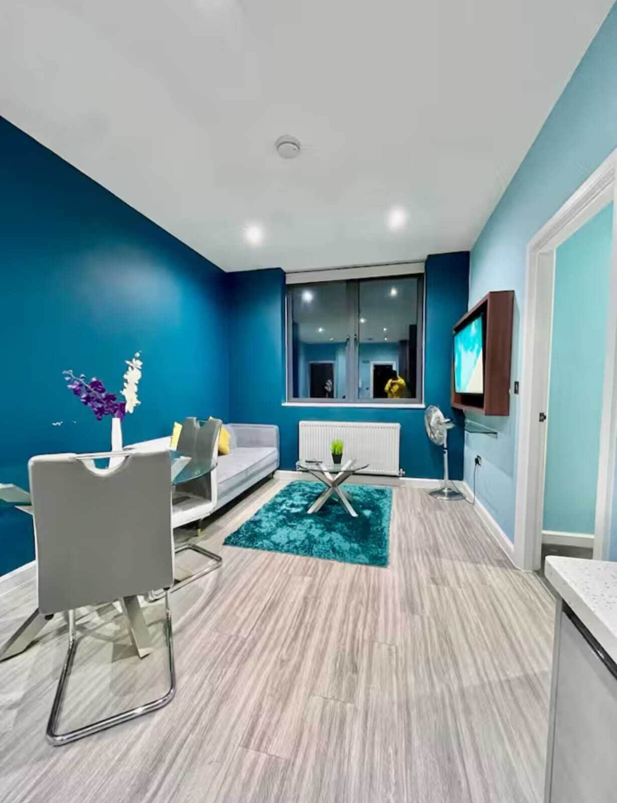 A modern living room with a grey sofa, a glass coffee table, and a blue accent wall.