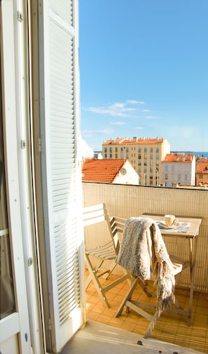 En balkon med bord, stole og udsigt til bygninger og havet.
