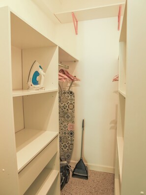 A closet with shelves, an ironing board, a broom, and hanging clothes. - Spacious 3-bedroom apartment in delightful Cannes with AC - LES BANANIERS (Cannes)