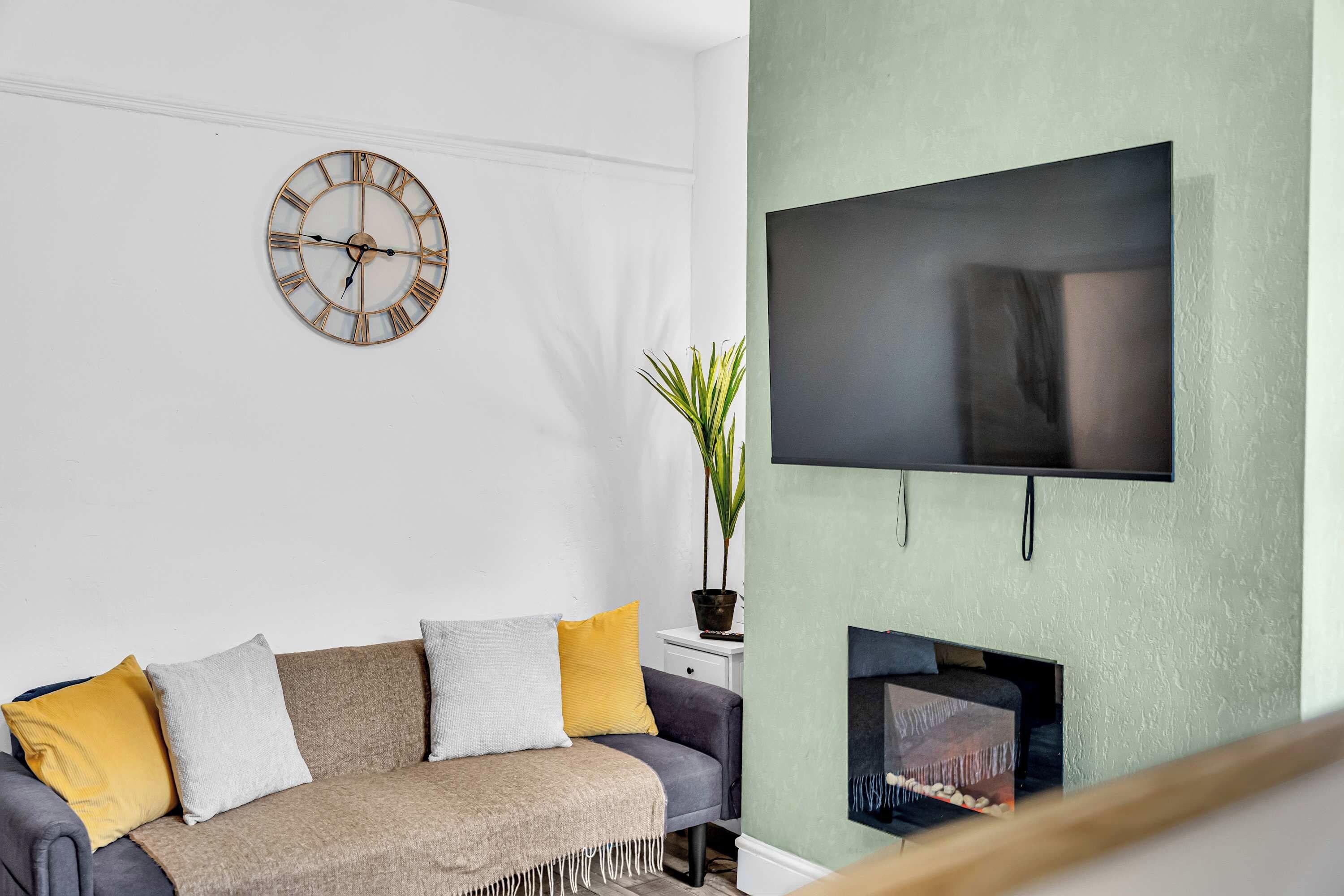 A living room with a sofa, a wall-mounted TV, and a decorative clock.