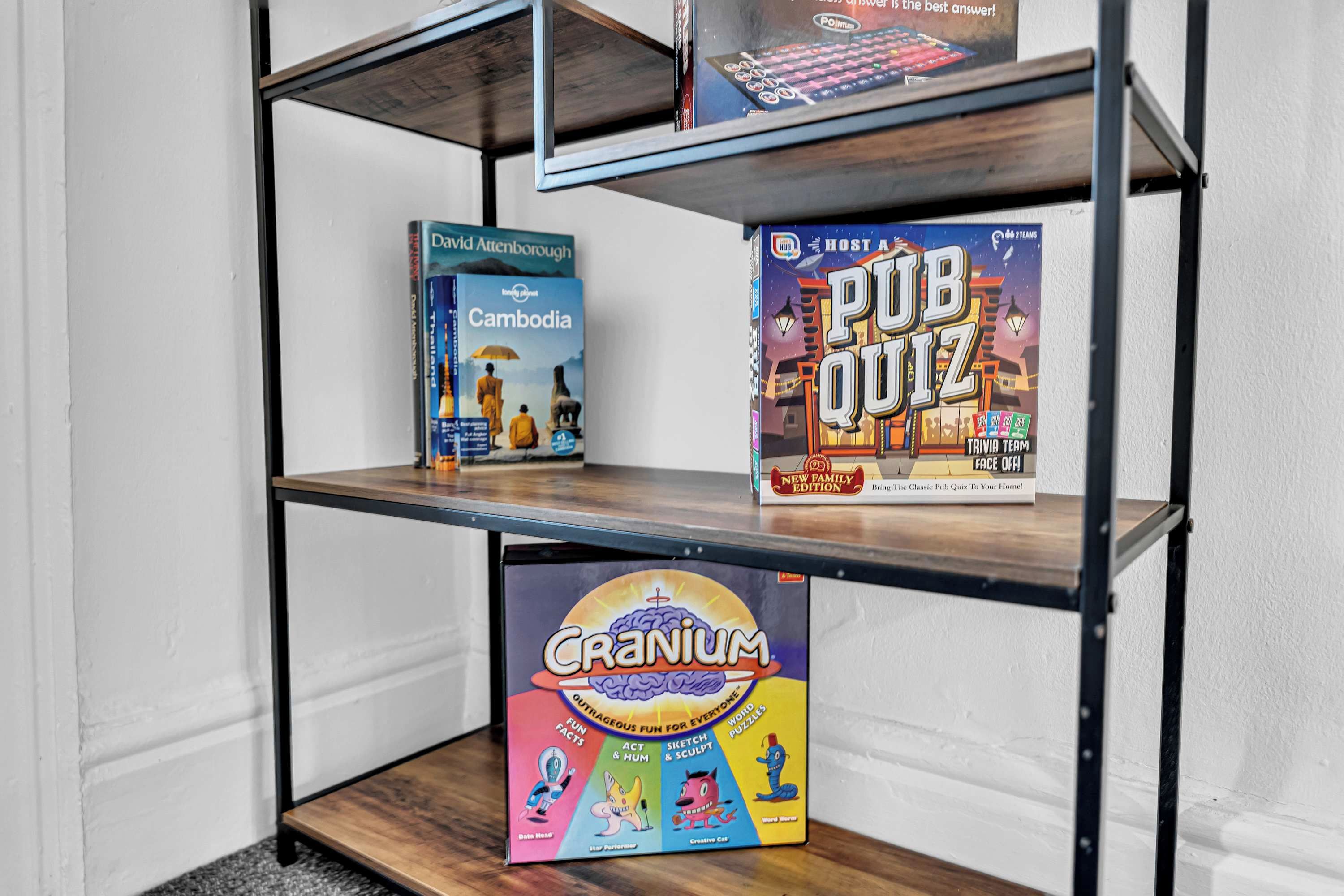 A bookshelf with three books: 'Cambodia' by David Attenborough, 'PUB Quiz' trivia game, and 'Cranium' family game.
