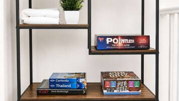 A wooden bookshelf with three shelves, holding books, a board game, and a potted plant.