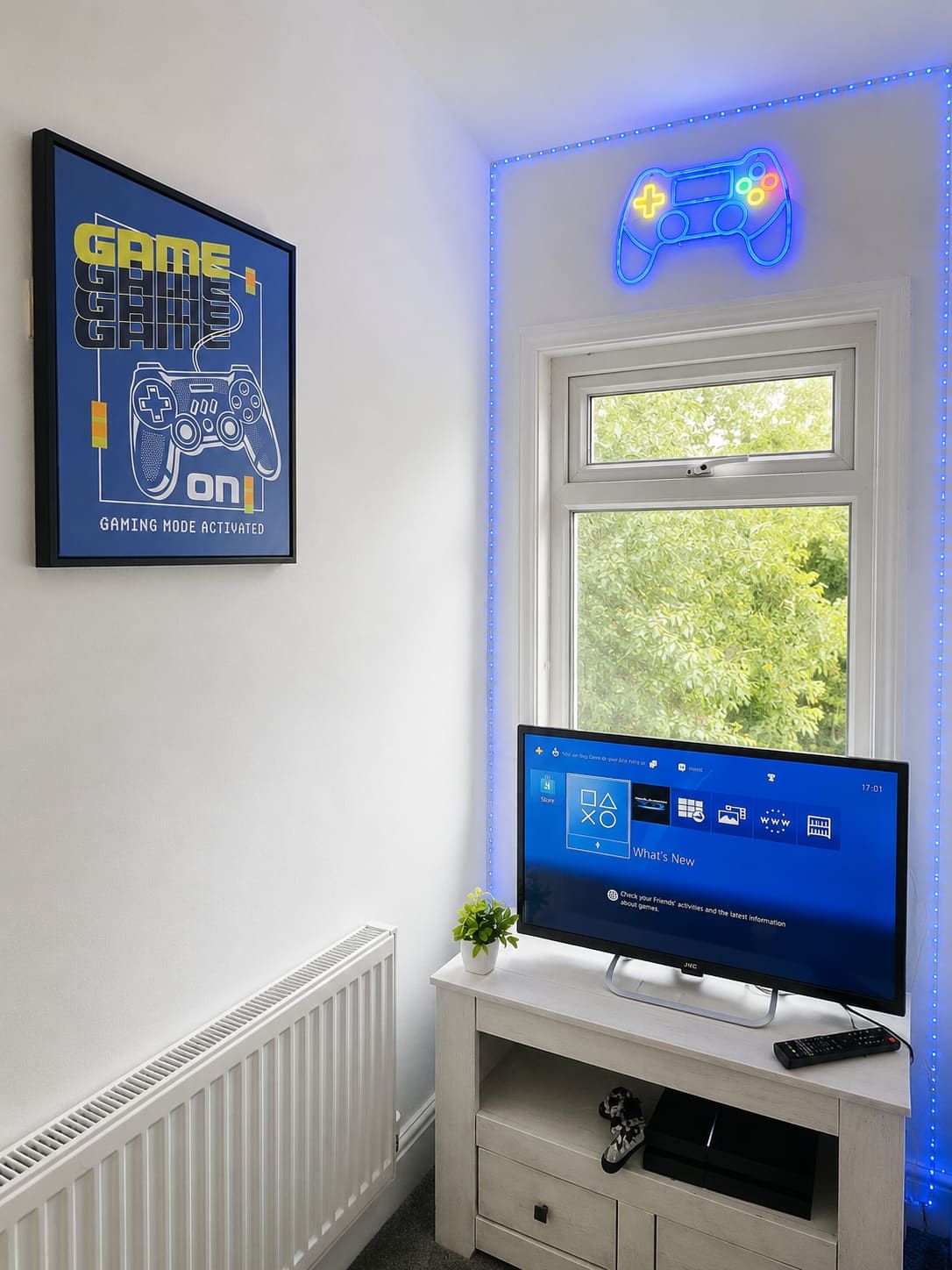 Une pièce décorée avec des œuvres d’art murales sur le thème des jeux vidéo, une fenêtre donnant sur un paysage verdoyant et un téléviseur diffusant une chaîne d’information.