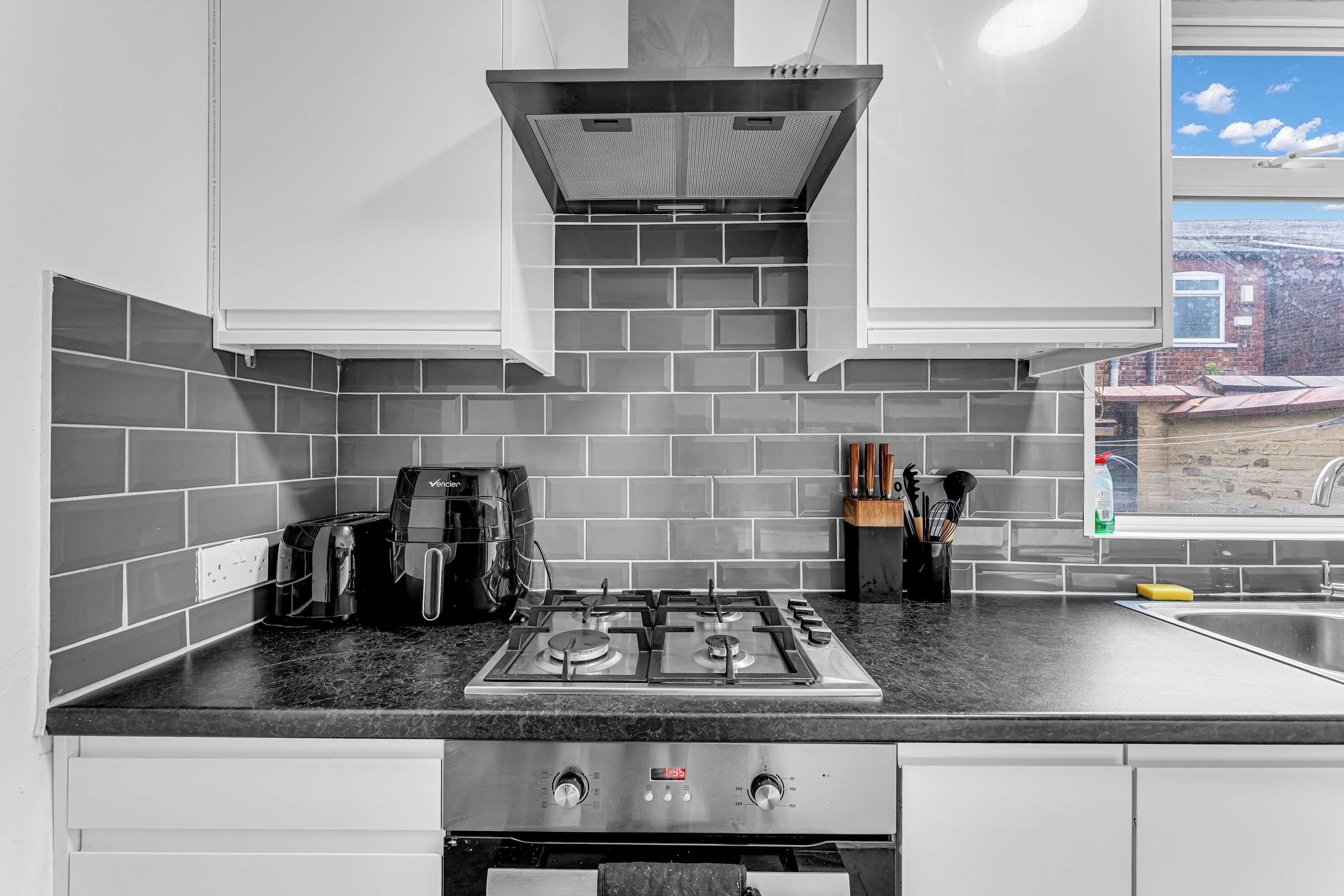 A modern kitchen with a gas stove, a coffee maker, and a view of the outside.