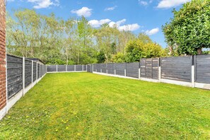 A fenced backyard with a grassy lawn and trees in the background. - Modern 3 Bed Home | Driveway | Spacious Garden (Stretford)