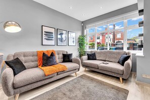 A living room with two grey sofas, a large window, and framed artwork on the wall. - Modern 3 Bed Home | Driveway | Spacious Garden (Stretford)