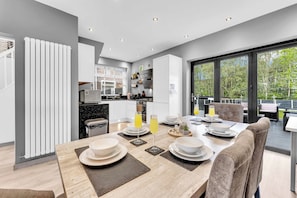 A modern kitchen with a dining area, large windows, and a view of greenery. - Modern 3 Bed Home | Driveway | Spacious Garden (Stretford)
