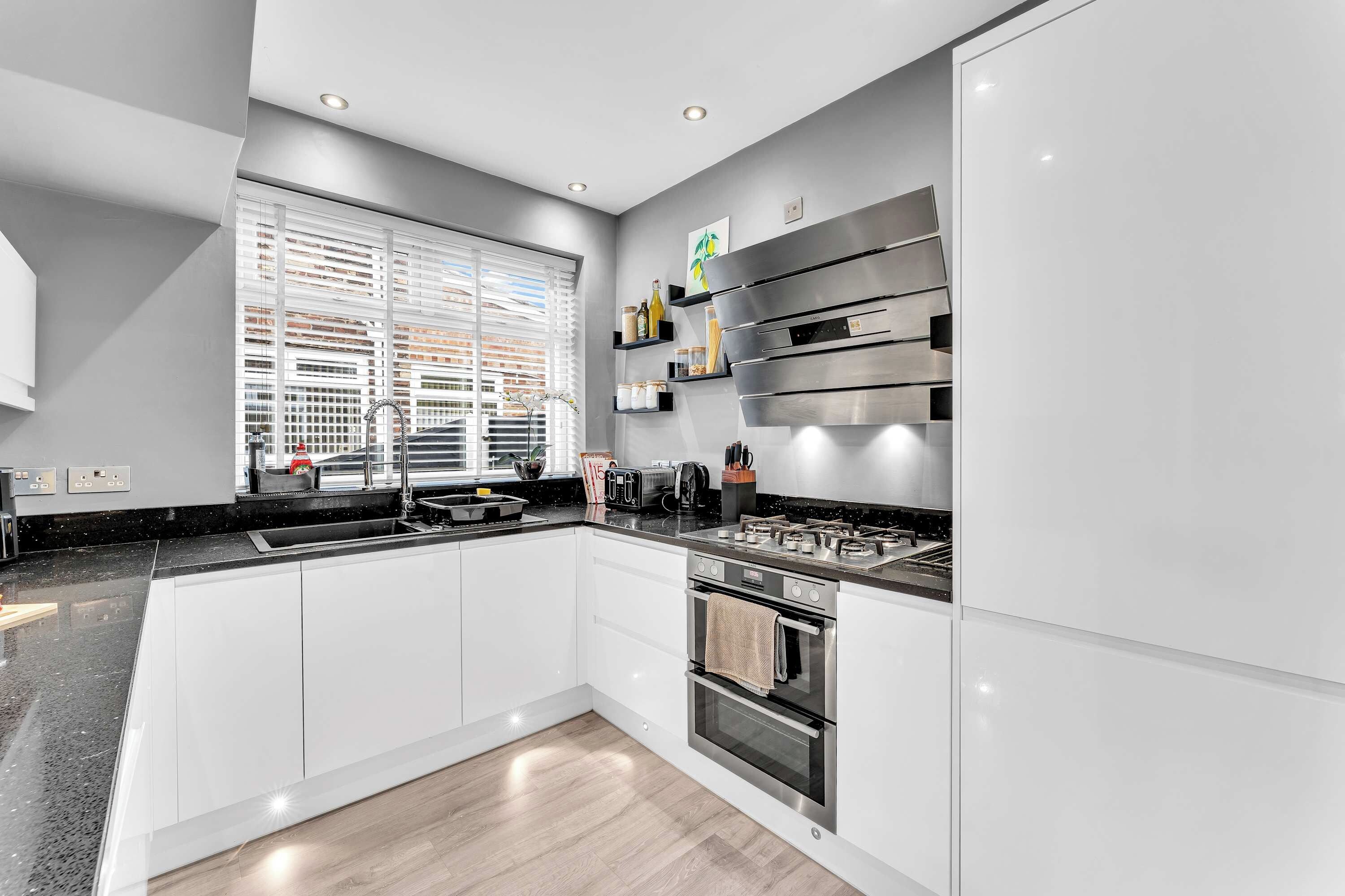 Cocina moderna con horno empotrado, estufa y ventana con persianas.