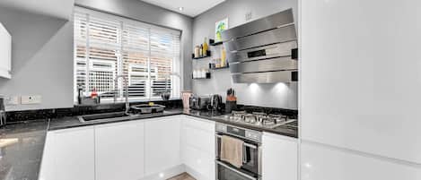 Cocina moderna con horno empotrado, estufa y ventana con persianas.