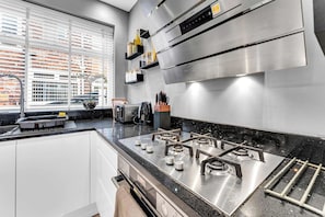 A modern kitchen with a gas stove, a built-in oven, and a window overlooking a cityscape. - Modern 3 Bed Home | Driveway | Spacious Garden (Stretford)