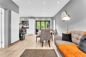 A modern living room with a sofa, a dining area, and a kitchen. - Modern 3 Bed Home | Driveway | Spacious Garden (Stretford)
