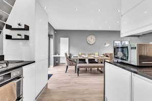 A modern kitchen with a dining area, featuring a clock, built-in appliances, and a minimalist design. - Modern 3 Bed Home | Driveway | Spacious Garden (Stretford)