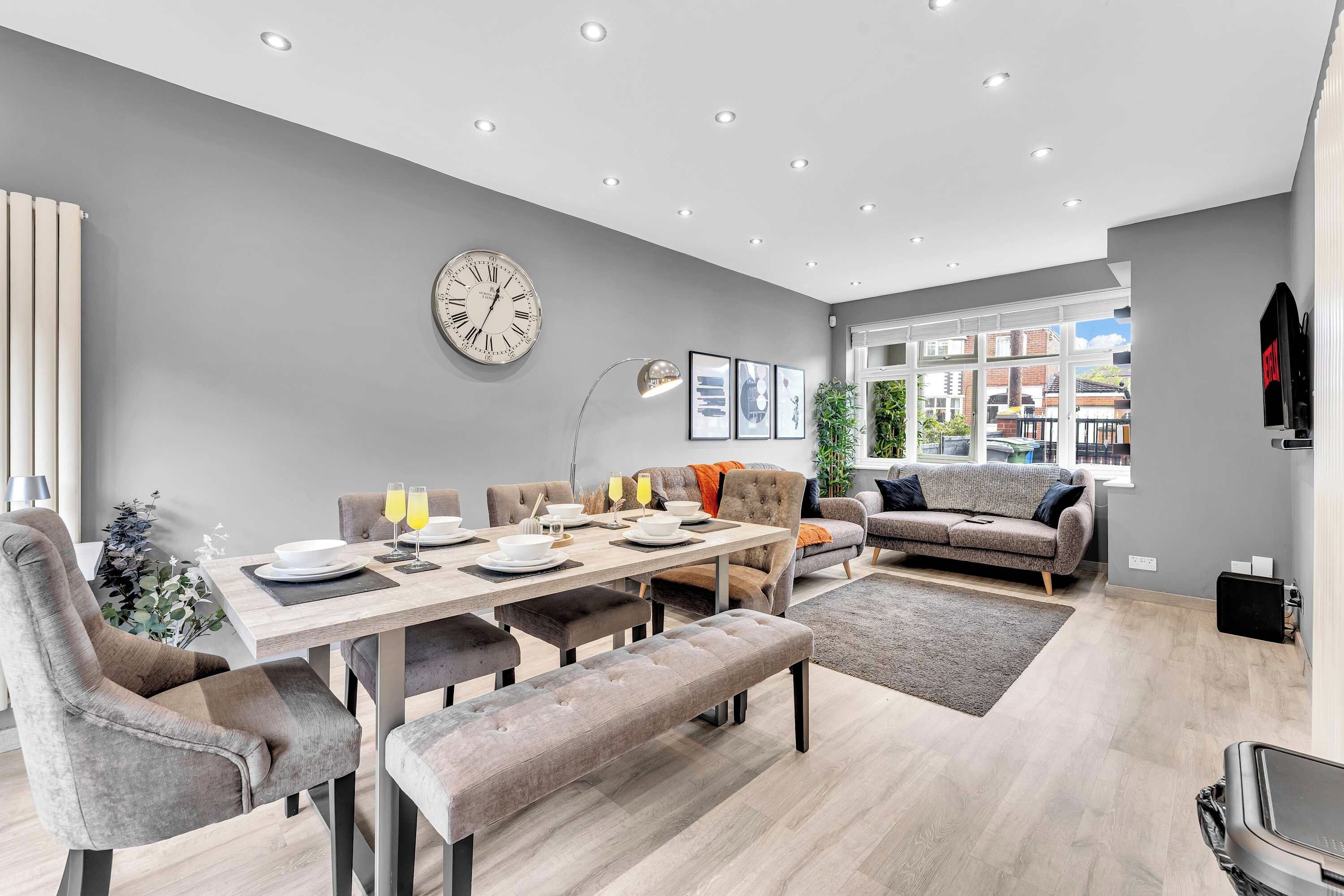 A modern living room with a dining area, grey walls, and a large window.