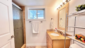A bathroom with a shower, a window, a sink with a vanity, and a mirror with lights. - The Lakeplace on Flathead close to GNP (Polson)