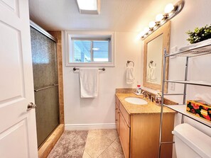 Een badkamer met een douche, een raam, een wastafel met kastje en een spiegel met verlichting.